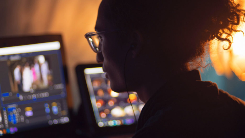 A woman sits at a desk looking at multiple computer screens.