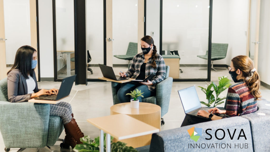 Three women in masks are seen sitting inside the newly opened SOVA Innovation Hub space.