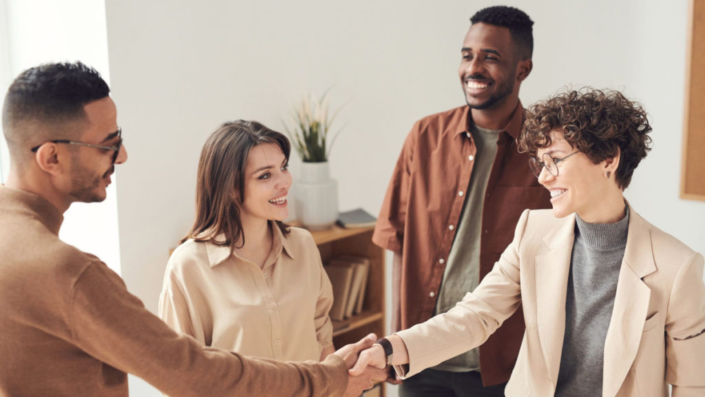 A group of four colleagues stand together, with two people shaking hands.