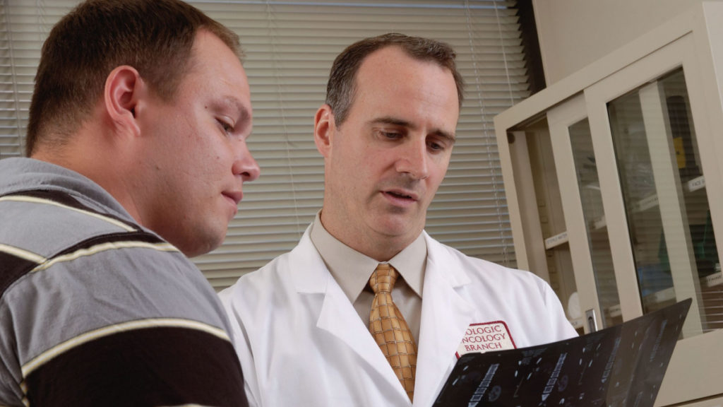 Two men, a doctor and a patient, sit in an examination room looking at an X-ray.