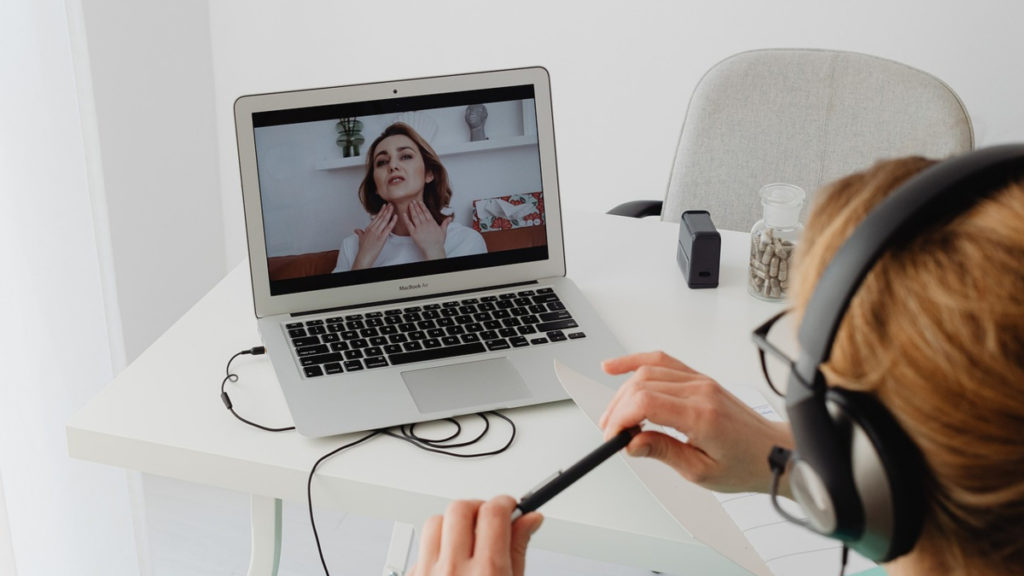 What is telemedicine? A healthcare practitioner speaks to a patient via videoconferencing. The patient is holding her hands up to her throat as she describes her symptoms.