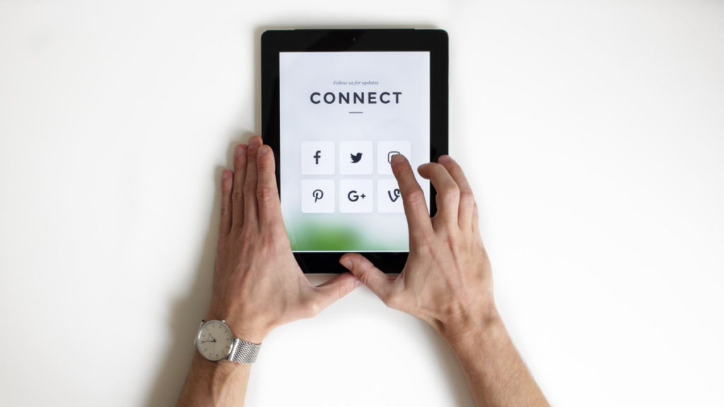 A pair of hands holds a tablet. The screen reads CONNECT and shows different social media icons.