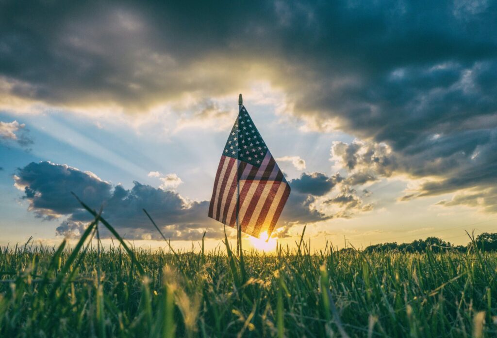 image of American flag in field of grass with sun behind it