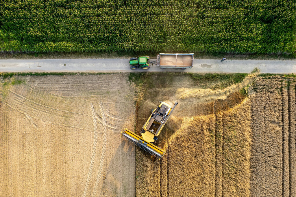 Aerial view of a combine harvester and grain wagon working across multiple crop fields during harvest.
