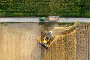 Aerial view of a combine harvester and grain wagon working across multiple crop fields during harvest.